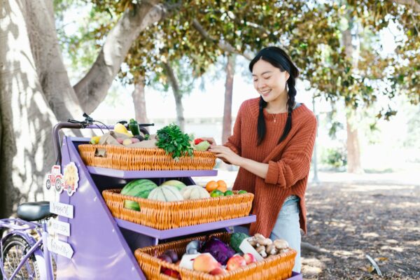 Woman in sweater selecting fresh produce at outdoor market fruit stand.